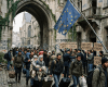 Migrants with luggage walking past protesters holding signs about migration crisis and Europe