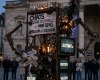 Mechanical sculpture with screens showing words 'Légitimité,' 'Prestige,' 'Valeurs,' and signs with 'Prestige,' 'Tradition,' and 'Culture' surrounded by people.