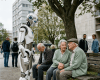 Humanoid robot standing and communicating with elderly couple sitting on a bench in a park